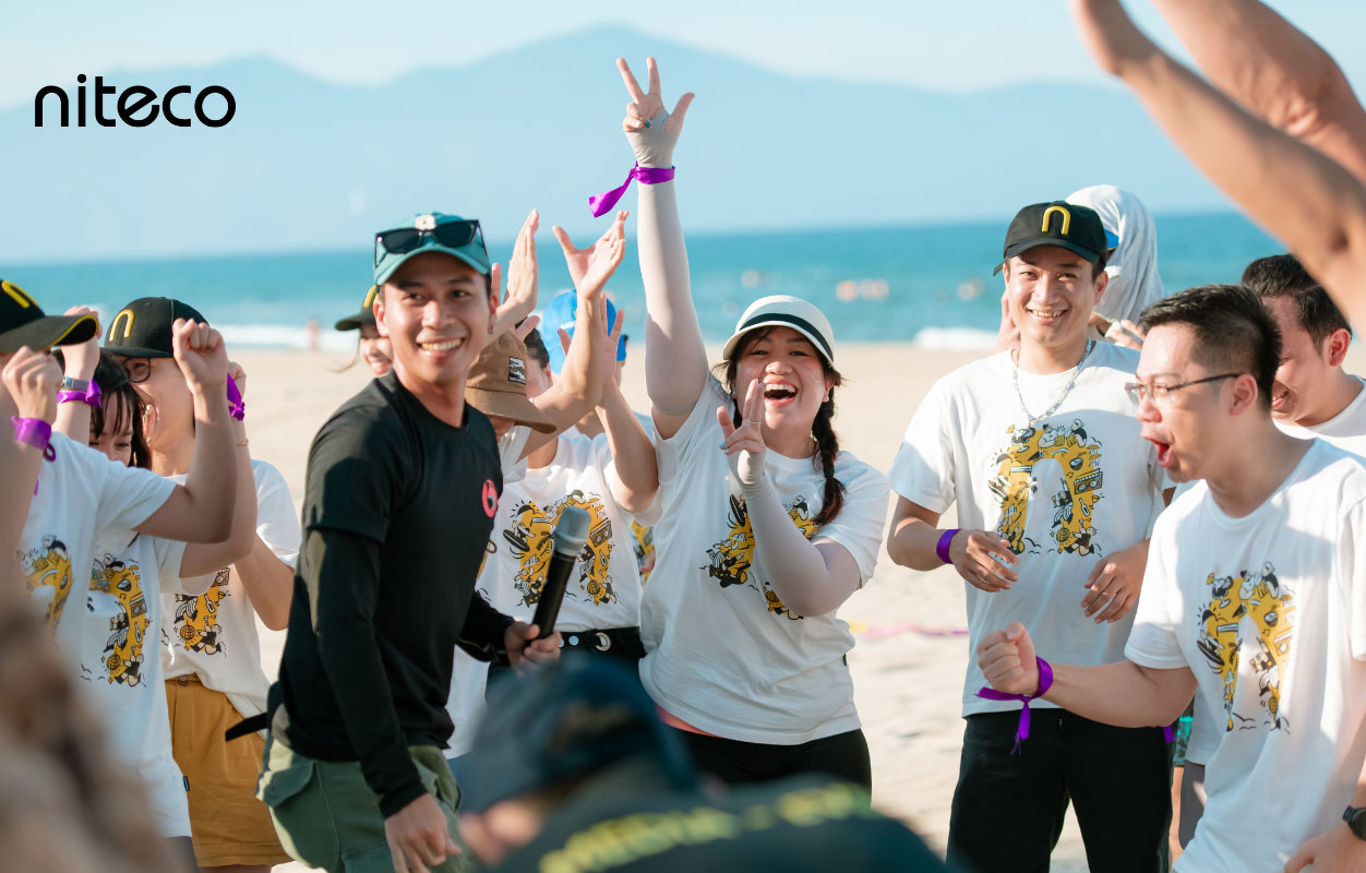 Niteco team celebrating on beach during outdoor team-building event with cheer