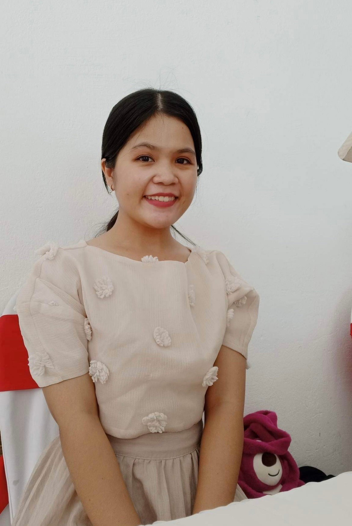 Smiling young woman in a beige dress with floral details, sitting indoors