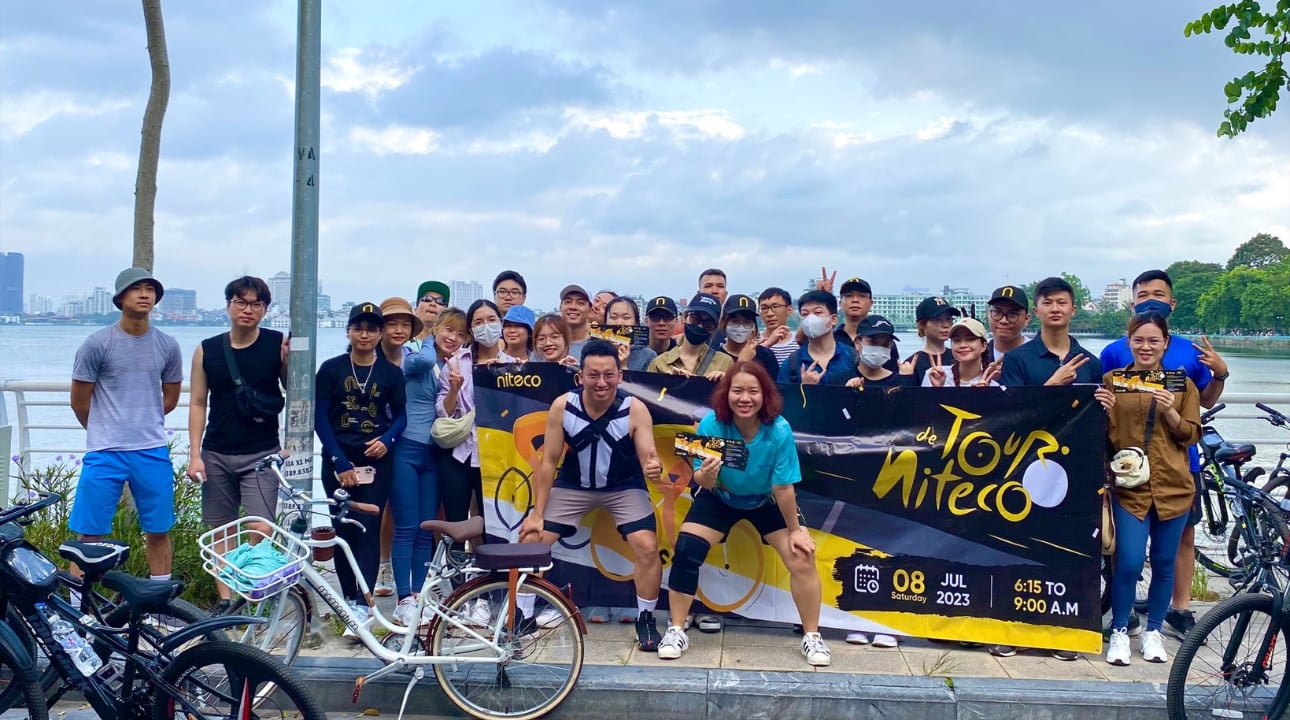 Niteco cycling Tour participants posing by lakeside with bikes and event banner