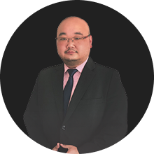 Professional portrait of a man in a black suit and pink tie on a dark background