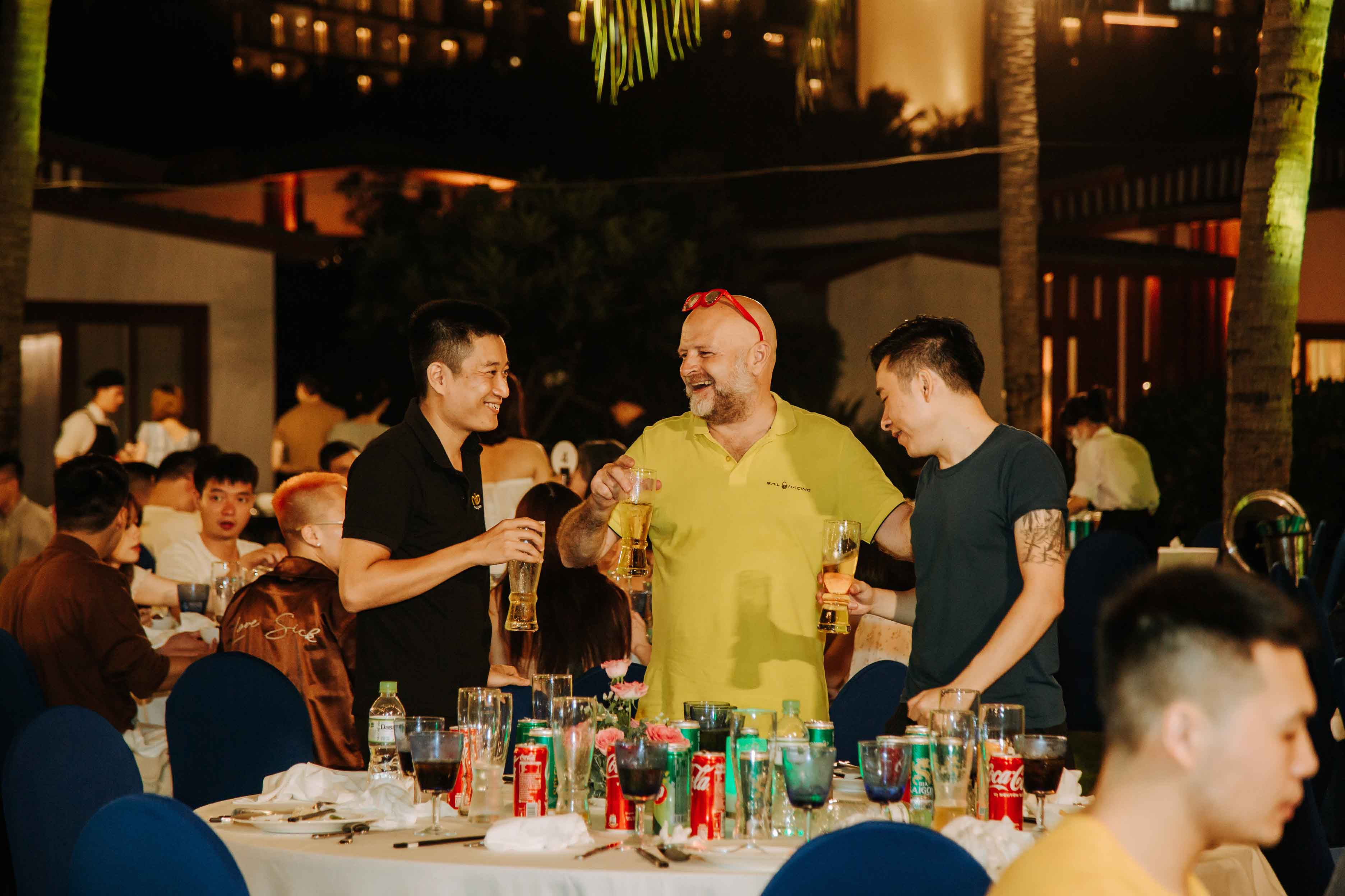 Three men toasting with drinks at a lively rooftop bar gathering at night