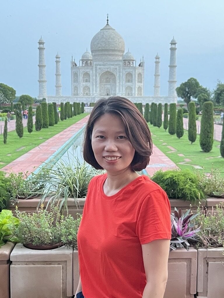 Woman in red shirt smiling with Taj Mahal and gardens in background at Agra