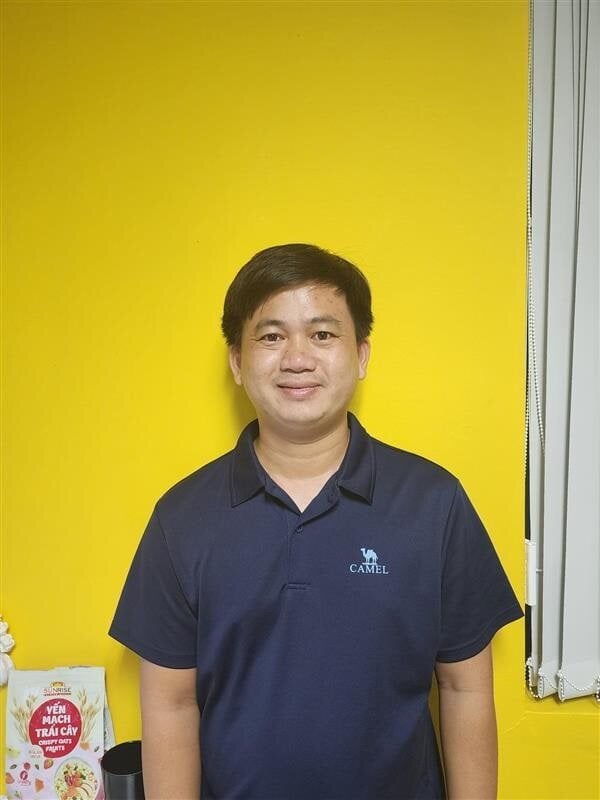 Man wearing navy blue Camel polo shirt standing against yellow wall with cereal box