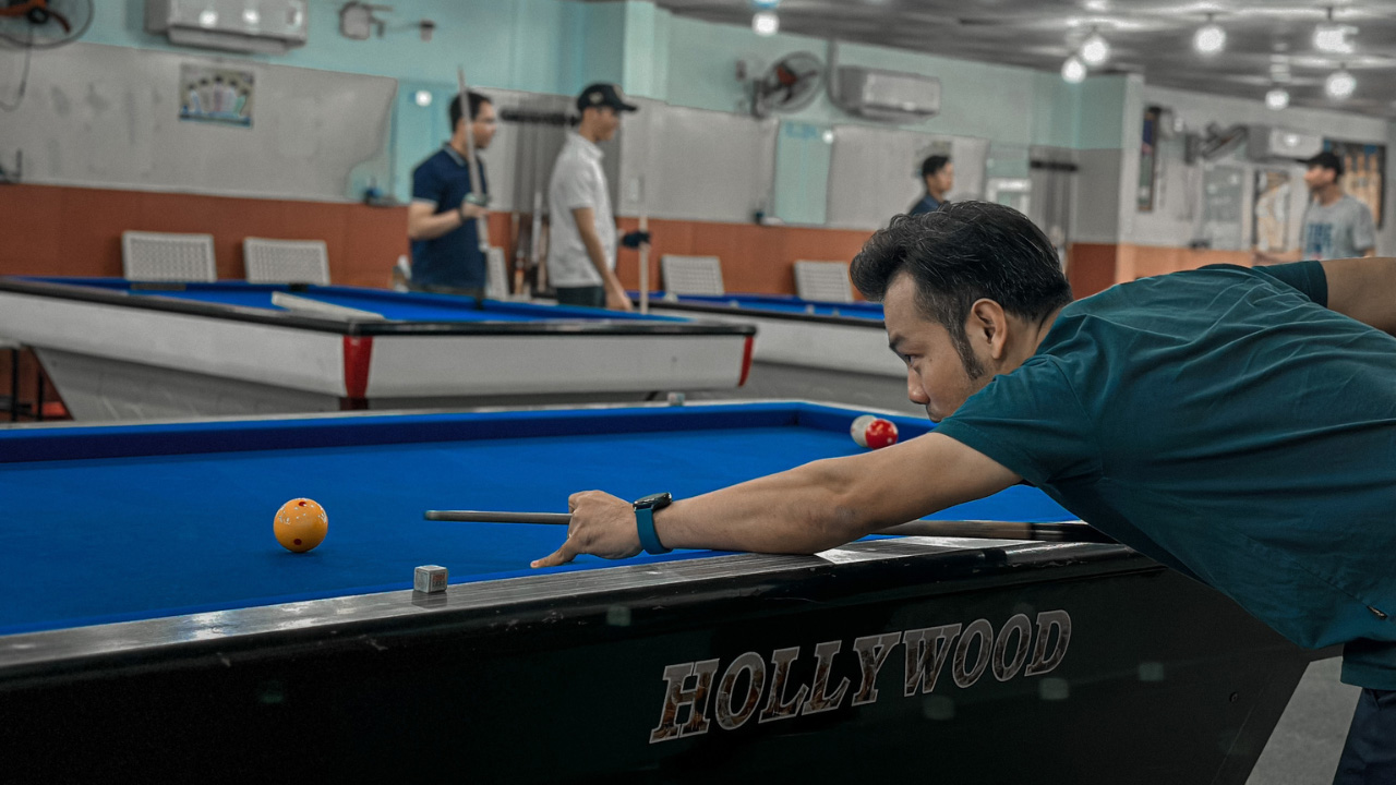Man aiming a shot on Hollywood billiard table in a busy pool hall