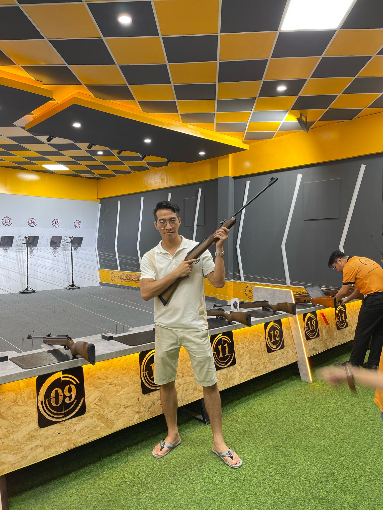 Man holding rifle at indoor shooting range with numbered shooting lanes