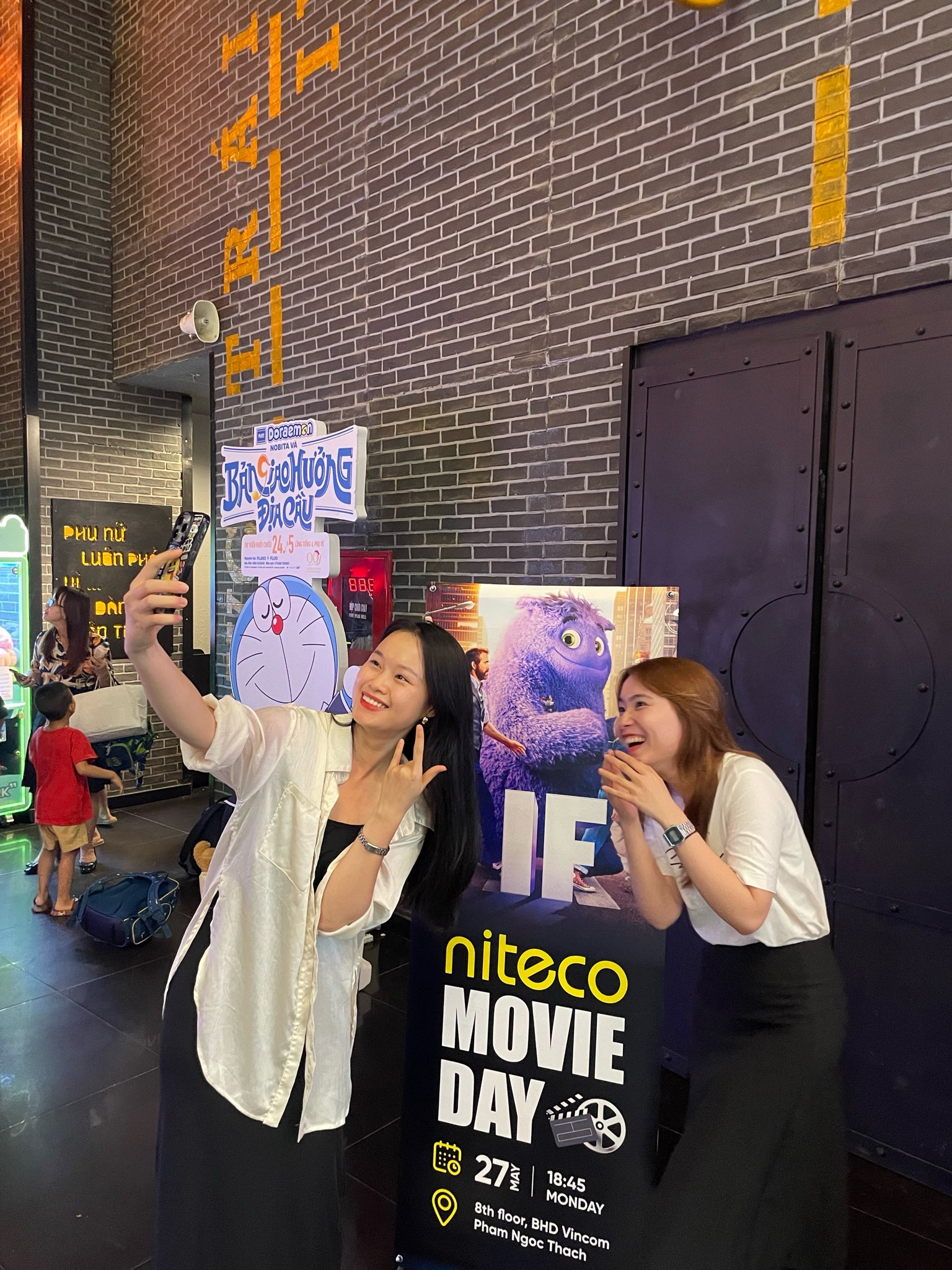 Two women taking a selfie at Niteco Movie Day event with animated movie posters