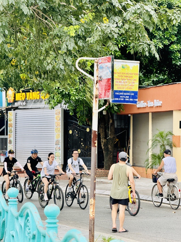 Cyclists riding along Hoang Thanh Thang Long road under green trees in Hanoi