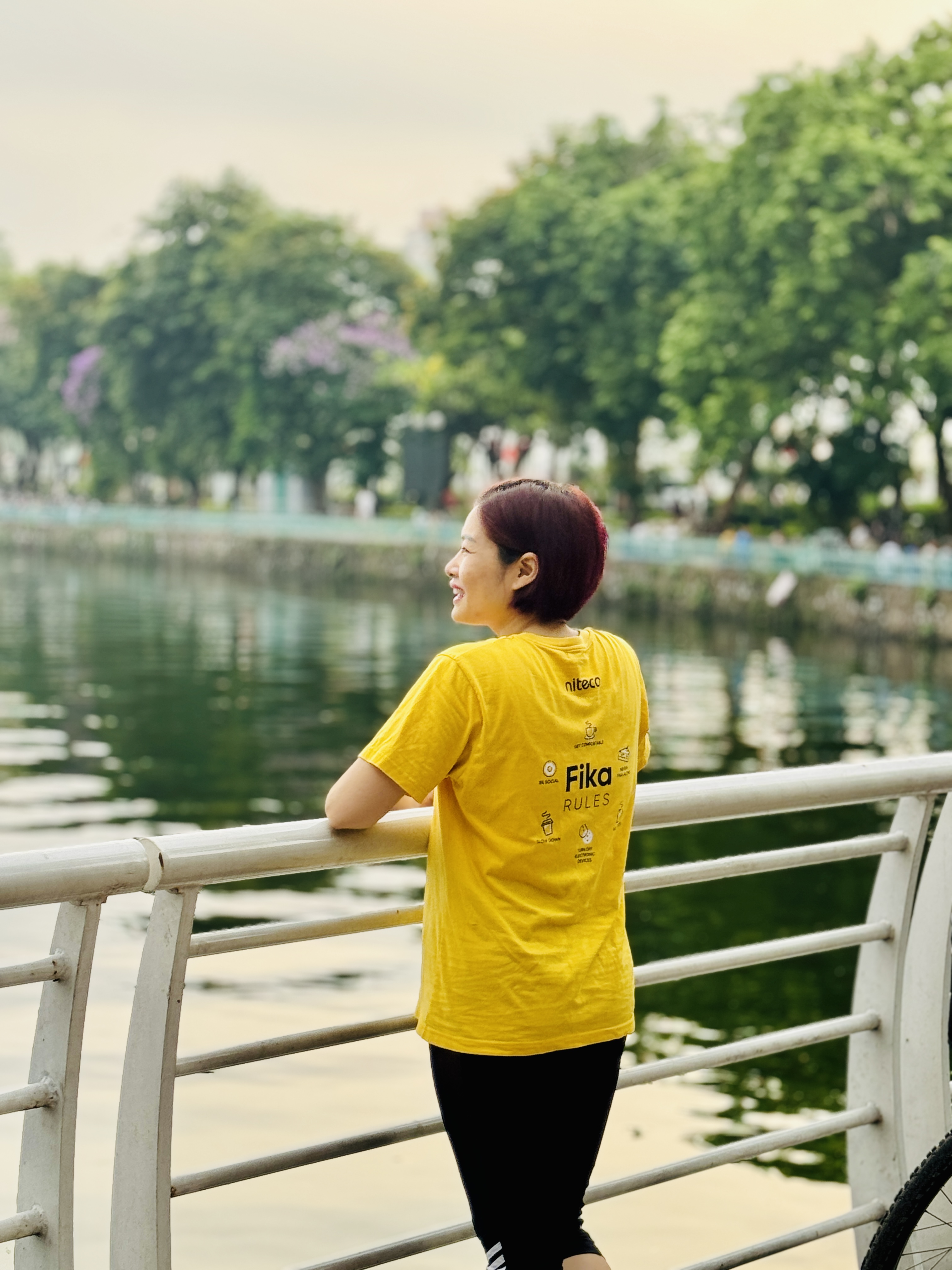 Woman in yellow Fika Rules t-shirt enjoying lakeside view by railings