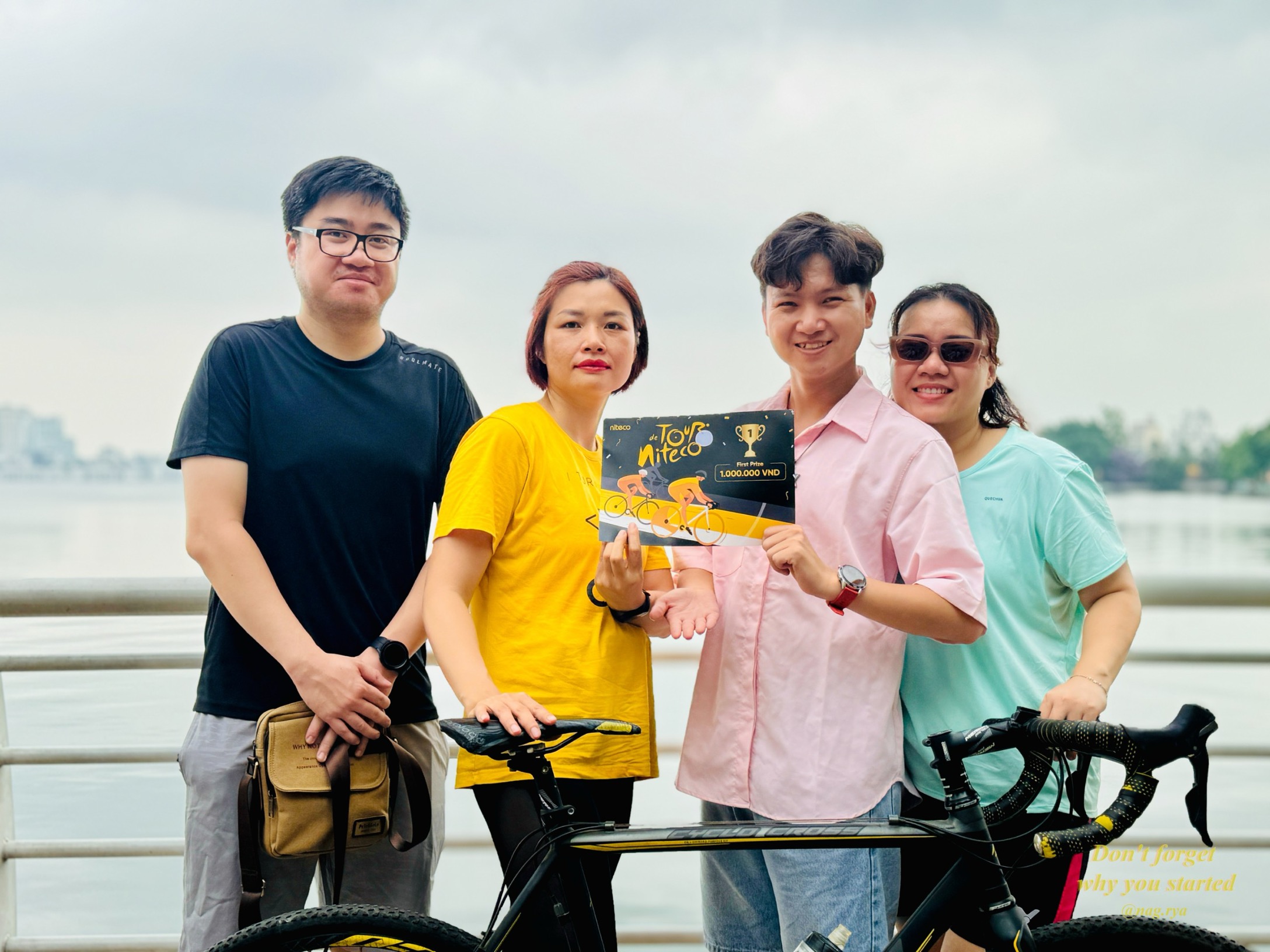 Niteco Tour winners holding prize certificate by the bike near water railing