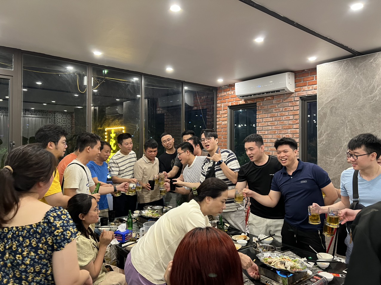 Group of friends toasting beer at a festive party with hot pot dinner indoors