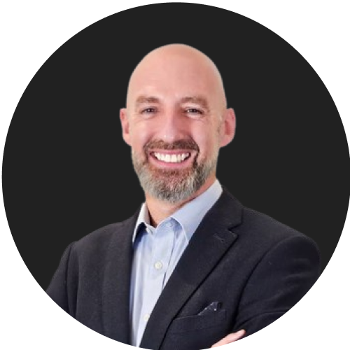 Bald bearded man smiling and wearing a black suit.