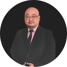 Professional headshot of a man in a black suit and pink tie on a dark background