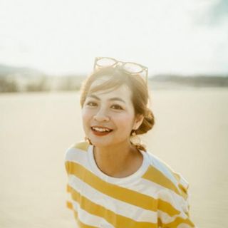 Young woman in yellow striped shirt smiling outdoors with glasses on her head