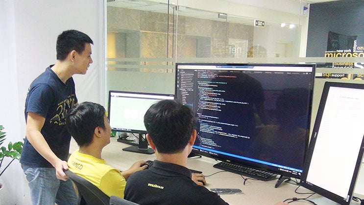 Developers collaborating on coding displayed on large monitors in modern office
