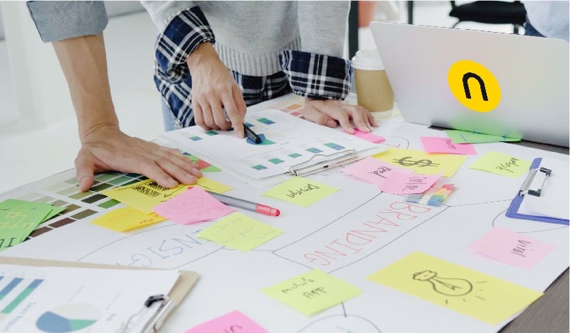 Hands analyzing branding charts and colorful sticky notes on a creative workspace