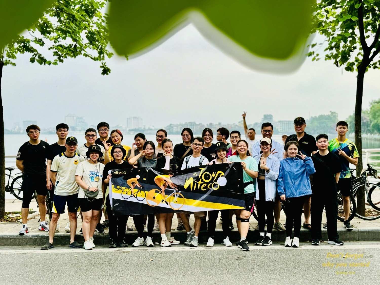 Group of cyclists holding Tour de Niteco banner by riverside during cycling event